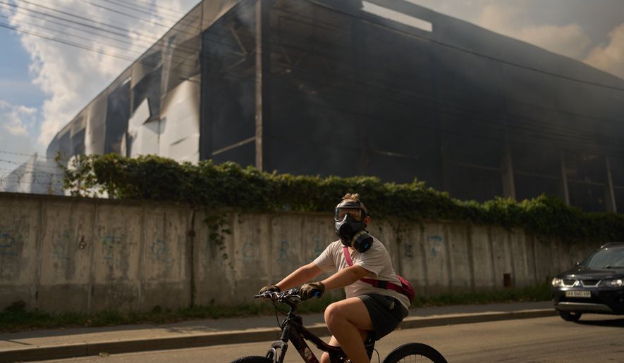 A local resident wears a gas mask as he rides a bicycle past a partially destroyed warehouse after a Russian drone attack in Brovary on the outskirts of Kyiv, Ukraine, Friday, Sept. 4, 2026. (AP Photo/Francisco Seco)