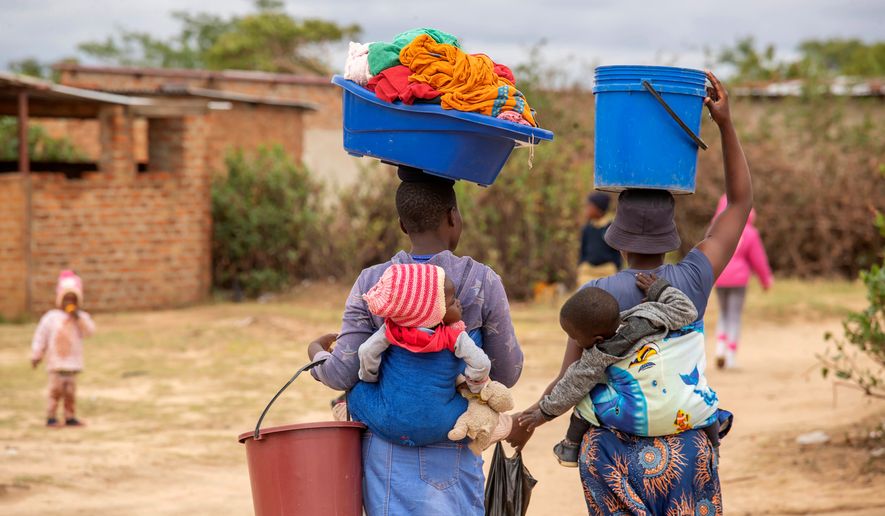 FILE - Women, with children on their backs, carry out chores in Epworth, Zimbabwe, on Nov. 14, 2024. (AP Photo/Aaron Ufumeli, File)