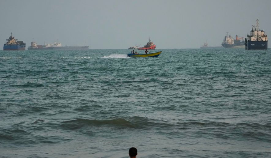 A swimmer remains near the shore as a motorboat passes commercial vessels anchored in the Strait of Hormuz off Bandar Abbas, Iran, Friday, Sept. 4, 2026. (AP Photo/Vahid Salemi)