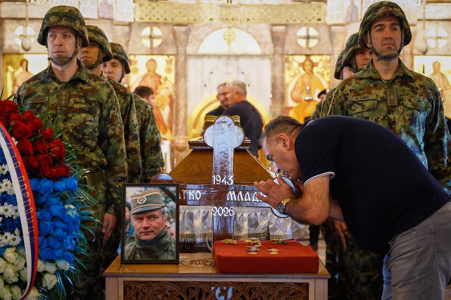 A man touches the cross as Serbian national military servicemen stand around the coffin of the former Bosnian Serb army commander Ratko Mladic, who died last week while serving a life sentence for genocide and other atrocities during the war in Bosnia, at the St. Luka Church, in Belgrade, Serbia, Monday, Sept. 7, 2026. (AP Photo/Marko Drobnjakovic)