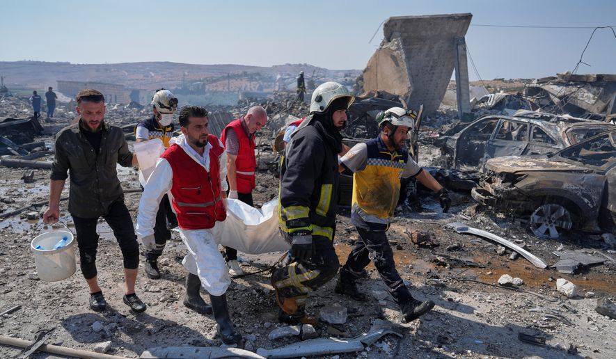 Civil defense workers and a firefighter remove a body from the site of an explosion at what Syria's Defense Ministry said was a warehouse used for the temporary storage of weapons near Sarmada, in Idlib province, Syria, Wednesday, Sept. 9, 2026. (AP Photo/Omar Albam)