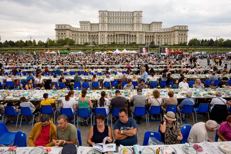 People sit at a 5-kilometer (3.1 miles) long "Uniting Table", made from recycled materials, during a Guinness World Record event to raise money for a children's psychiatric facility, outside the communist-era built Palace of Parliament, in Bucharest, Romania, Saturday, Sept. 12, 2026. (AP Photo/Andreea Alexandru)