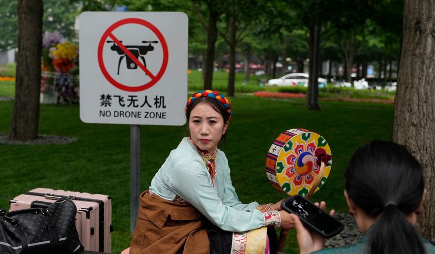 A performer rests near a "No Drone Zone" sign in Beijing, on May 31, 2023. (AP Photo/Ng Han Guan)