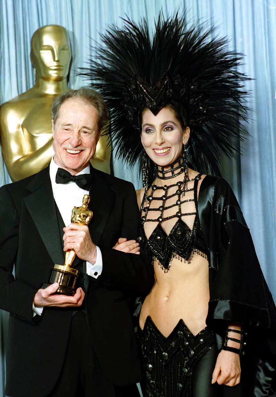 FILE - Actress-singer Cher wears a creation by designer Bob Mackie as she poses with actor Don Ameche after presenting him with the Oscar for best supporting actor at the Academy Awards in Los Angeles, March 24, 1986. (AP Photo/Lennox McLendon, File)