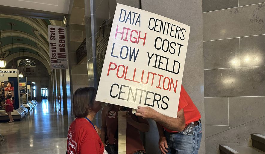 This photo taken with a smartphone shows opponents of data centers conversing behind a sign while preparing for a rally Wednesday, Sept. 16, 2026 at the Missouri Capitol in Jefferson City, Mo. (AP Photo/David A. Lieb)