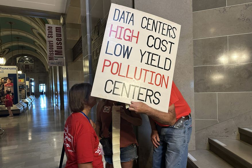 This photo taken with a smartphone shows opponents of data centers conversing behind a sign while preparing for a rally Wednesday, Sept. 16, 2026 at the Missouri Capitol in Jefferson City, Mo. (AP Photo/David A. Lieb)