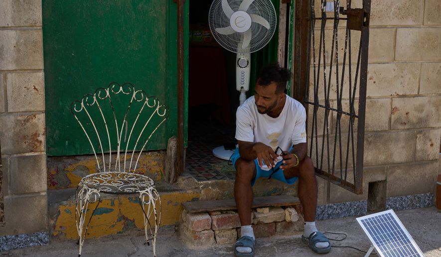 A man charges his fan's battery at his doorway using a small solar panel set up on the street during a blackout in Havana, Cuba, Friday, Sept. 18, 2026. (AP Photo/Ramon Espinosa)