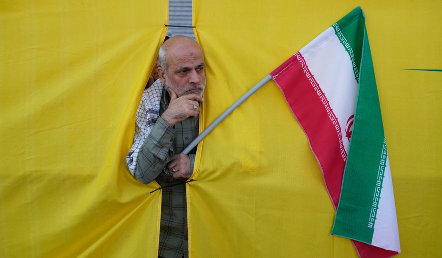 A man holding an Iranian flag peers through an opening in a curtain during the state-organized “Janfada,” or “Sacrifice for Iran,” military-style parade in Tehran, Iran, Friday, Sept. 18, 2026. (AP Photo/Vahid Salemi)
