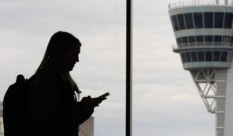 A traveler with a smartphone walks past an air traffic control tower at Philadelphia International Airport in Philadelphia on March 27, 2026. (AP Photo/Matt Rourke, File)