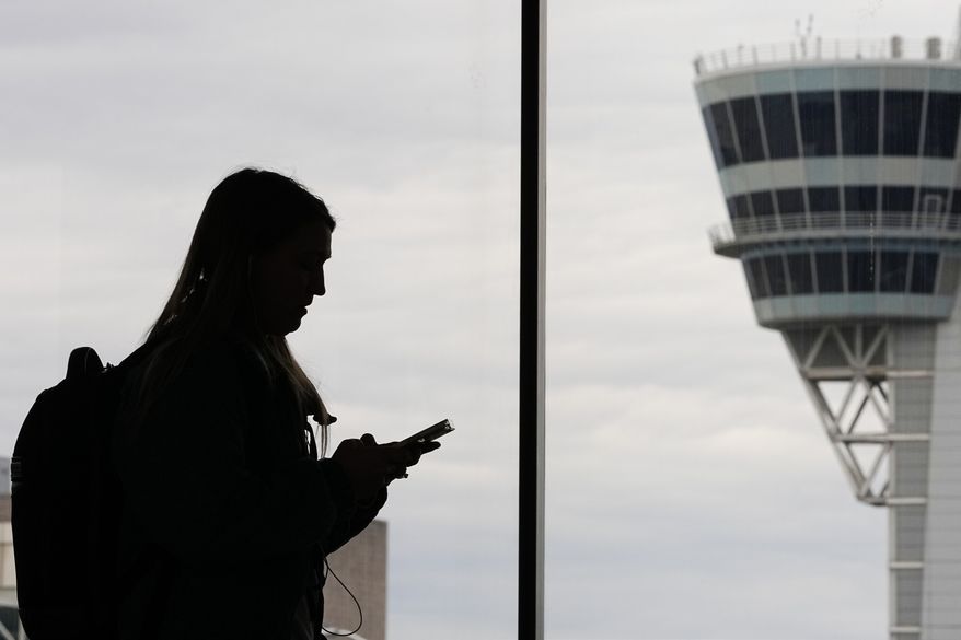 A traveler with a smartphone walks past an air traffic control tower at Philadelphia International Airport in Philadelphia on March 27, 2026. (AP Photo/Matt Rourke, File)