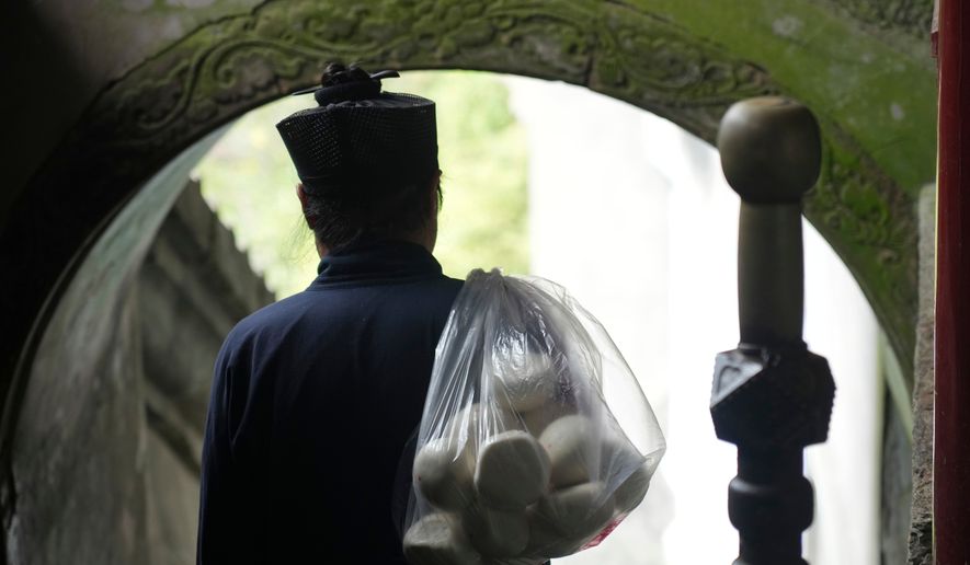 A Taoist priest walks with a bag of buns over his shoulder near the Golden Hall in Wudang Mountains in central China's Hubei Province on Sept. 3, 2026. (AP Photo/Achmad Ibrahim)