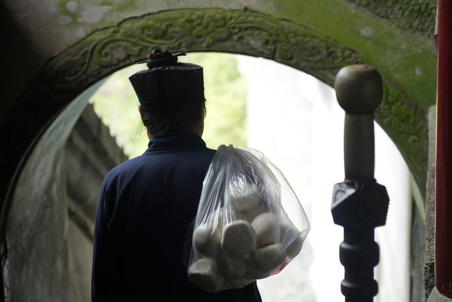 A Taoist priest walks with a bag of buns over his shoulder near the Golden Hall in Wudang Mountains in central China's Hubei Province on Sept. 3, 2026. (AP Photo/Achmad Ibrahim)