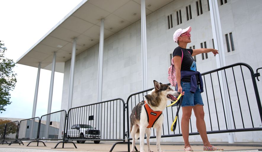 Quynh Pham of Washington, and her dog Jay, look at the Kennedy Center which has been fenced off and closed to the public, Thursday, Sept. 17, 2026, in Washington, "My husband and I moved to this neighborhood because we are big opera and ballet fans," says Pham, "we know the NSO players who live in the neighborhood, here you know exactly who is being affected." (AP Photo/Jacquelyn Martin)