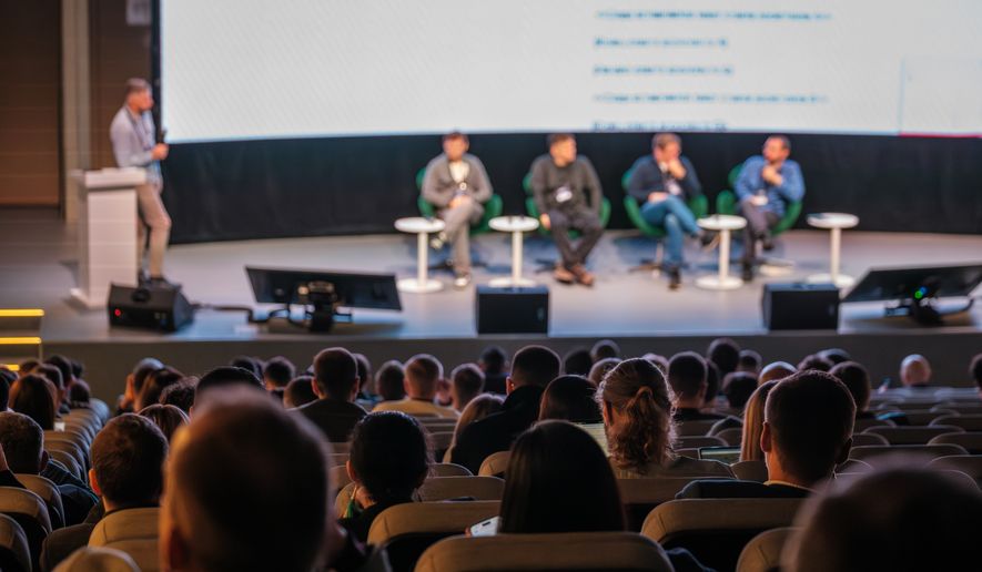 Audience watches panelists on stage during conference. File photo credit: Anton Gvozdikov via Shutterstock.