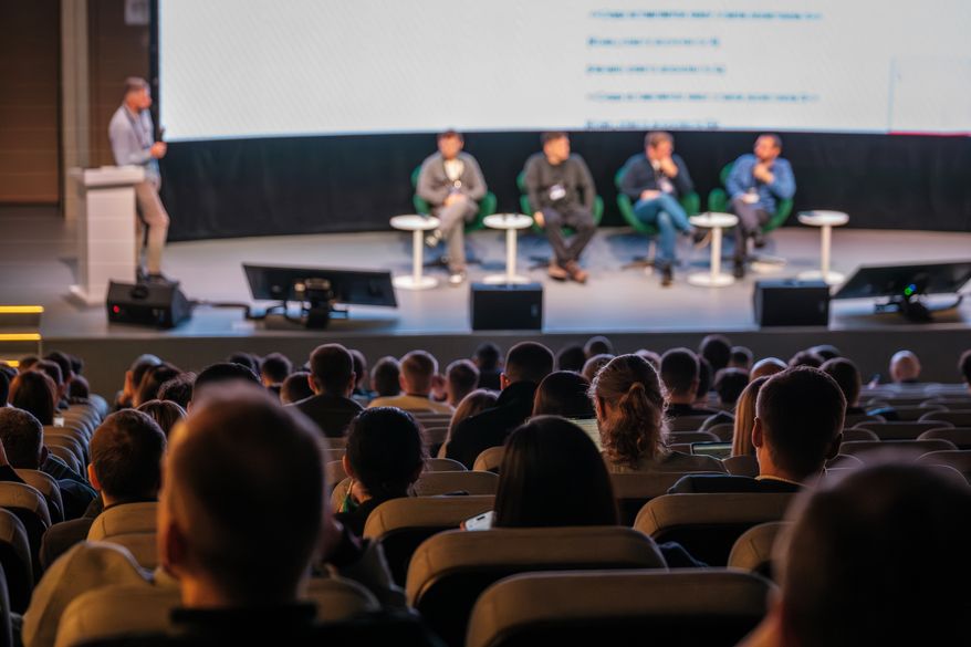 Audience watches panelists on stage during conference. File photo credit: Anton Gvozdikov via Shutterstock.