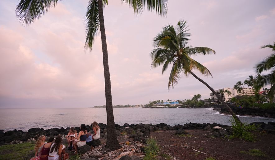 Members of Youth With A Mission read under a palm tree as Hurricane Nolo sits nearby Friday, Sept. 25, 2026, in Kona, Hawaii. (AP Photo/Gregory Bull)