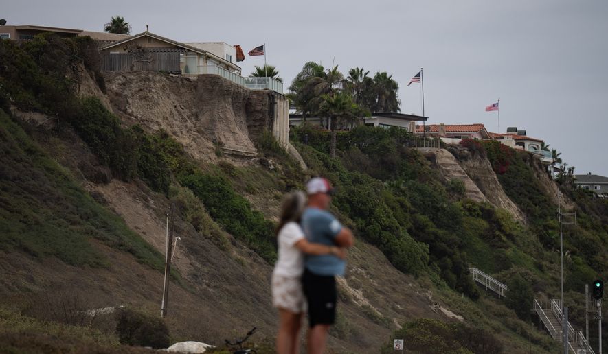 A couple hug at North Beach as crumbling seaside bluffs are seen behind them in San Clemente, Calif., Friday, Sept. 18, 2026. (AP Photo/Jae C. Hong)