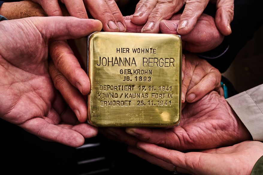 Relatives pose for a photograph holding a palm-sized brass Holocaust plaque in German reading, "Johanna Berger, born in 1893, lived here; deported on Nov. 17, 1941, murdered on Nov. 25, 1941 in Kowno/Kaunas Fort IX," by artist Gunter Demnig prior to the placing of the so called, "Stolperstein," or "Stumbling Blocks," in front of her former home in Berlin, Germany, May 6, 2026. (AP Photo/Markus Schreiber, File)