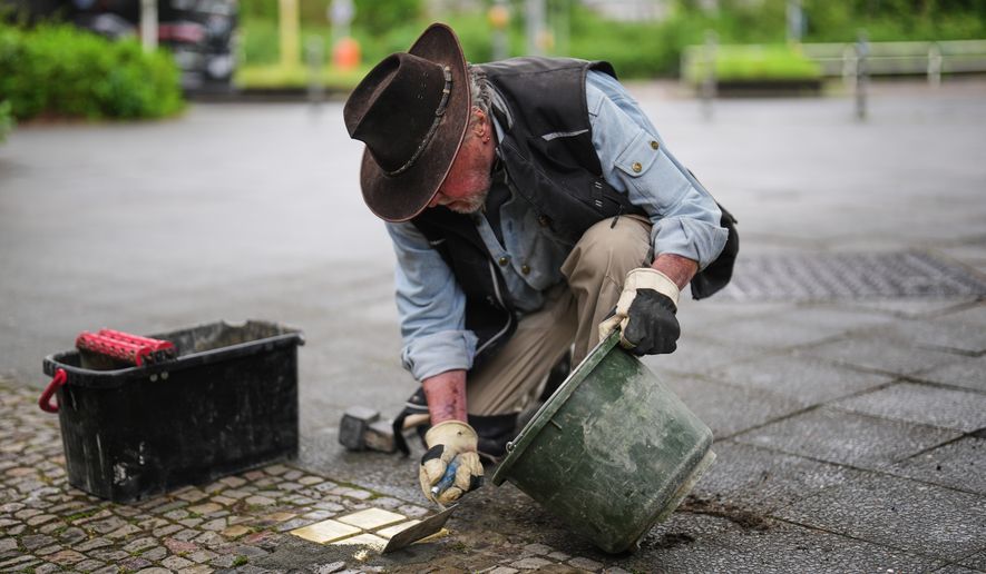 Artist Gunter Demnig places a palm-sized brass Holocaust plaques called, "Stolpersteine," or "Stumbling Blocks," with the names of victims of the Nazi regime in front of their former home at a street in Berlin, Germany, May 6, 2026. (AP Photo/Markus Schreiber, File)