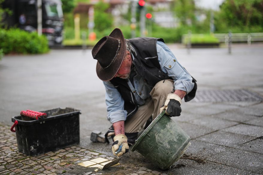 Artist Gunter Demnig places a palm-sized brass Holocaust plaques called, "Stolpersteine," or "Stumbling Blocks," with the names of victims of the Nazi regime in front of their former home at a street in Berlin, Germany, May 6, 2026. (AP Photo/Markus Schreiber, File)
