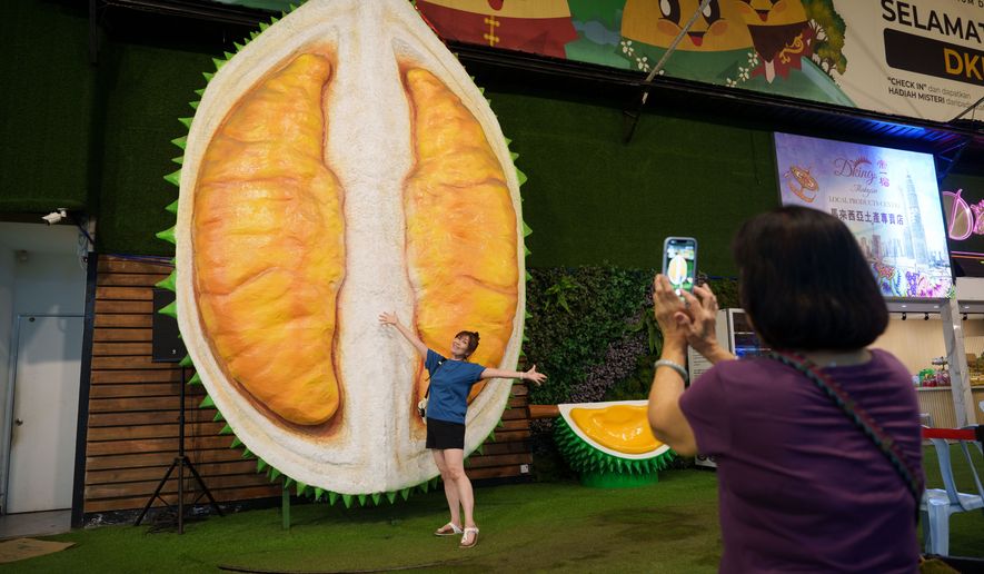A customer poses beside a giant durian display at a durian stall in Petaling Jaya, on the outskirts of Kuala Lumpur, Malaysia, Monday, June 22, 2026. (AP Photo/Vincent Thian)