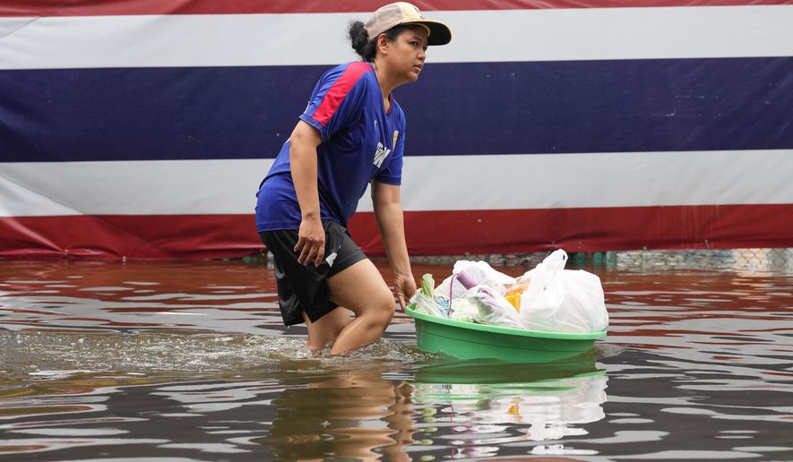A woman wades through floodwaters in front of a national flag after heavy rain in Bangkok, Thailand, Sunday, Sept. 27, 2026. (AP Photo/Sakchai Lalit)