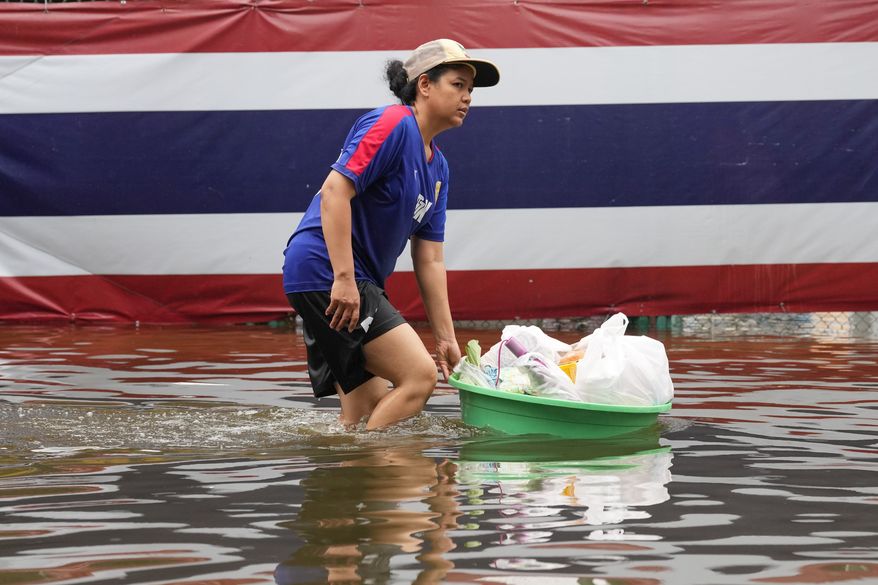 A woman wades through floodwaters in front of a national flag after heavy rain in Bangkok, Thailand, Sunday, Sept. 27, 2026. (AP Photo/Sakchai Lalit)