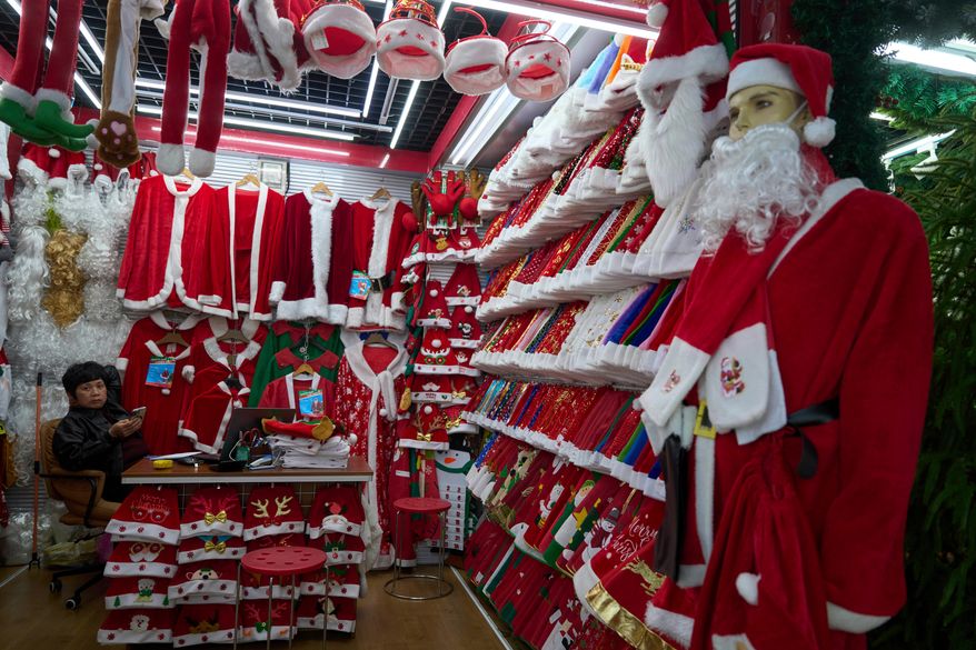 A vendor waits for customers near Santa costumes for sale at the Yiwu International Trade Market in Yiwu, eastern China's Zhejiang province on April 10, 2025. (AP Photo/Ng Han Guan, File)