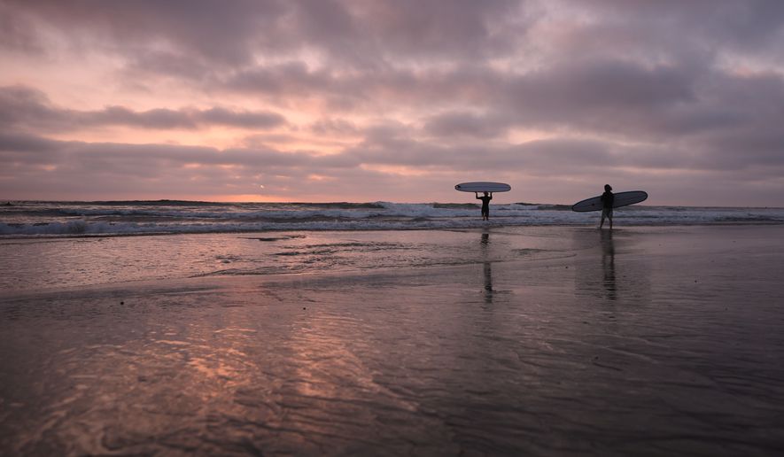 Surfers enter the Pacific Ocean as the sun sets Thursday, Oct. 1, 2026, in Encinitas, Calif. (AP Photo/Gregory Bull)