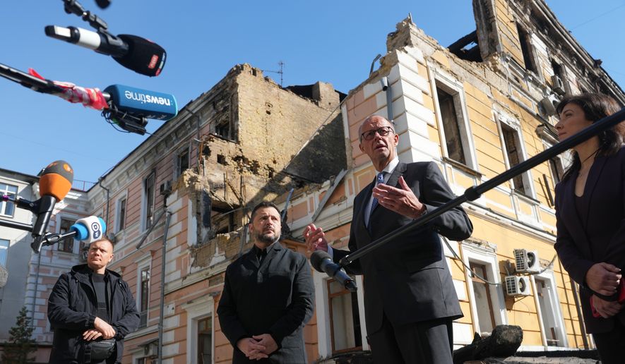 Ukraine's President Volodymyr Zelenskyy, centre, and German Chancellor Friedrich Merz speak to media with National Academy of science building damaged after a Russian drone strike, on the background, Kyiv, Ukraine, Sunday, Oct. 4, 2026. (AP Photo/Evgeniy Maloletka)