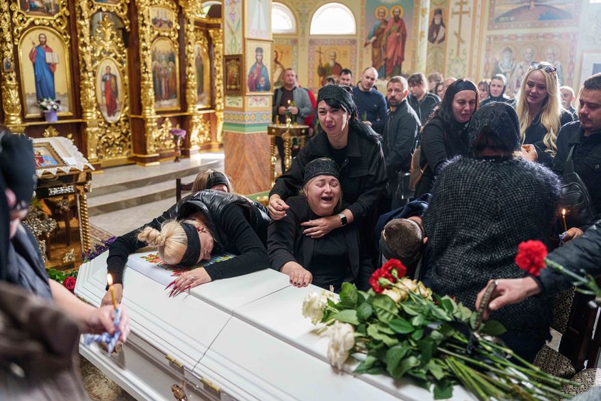 A mother surrounded by family cries sitting by the coffin of her son Illia Honcharenko, 14, killed by a Russian rocket strike on a residential house on Sept. 30, during their funeral, in Vyshhorod, Kyiv region, Ukraine, Friday, Oct. 2, 2026. (AP Photo/Evgeniy Maloletka)