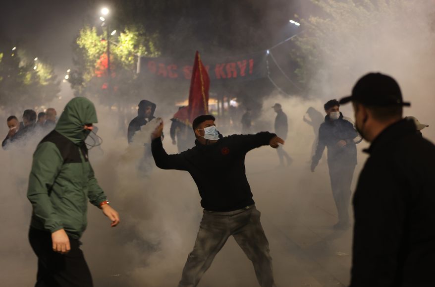 A protester throws back tear gas canisters at police units securing the entrance of the parliament building as protesters try to prevent Kosovo lawmakers from leaving the building without endorsing an amendment to the law on Specialist Chambers in Pristina, Kosovo, Monday, Oct. 5, 2026. (AP Photo/Visar Kryeziu)