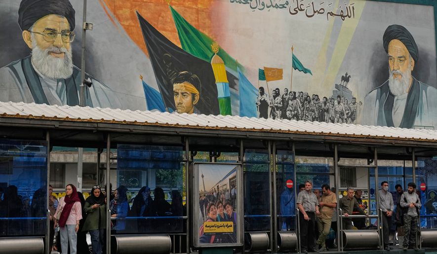 Commuters stand at a bus stop on Islamic Revolution street in front of a mural depicting the late Iranian revolutionary founder Ayatollah Khomeini, right, the late Supreme Leader Ayatollah Ali Khamenei, who was killed in the U.S. and Israel strike on Feb. 28, left, and Basij paramilitary forces, in Tehran, Iran, Tuesday, Oct. 6, 2026. (AP Photo/Vahid Salemi)