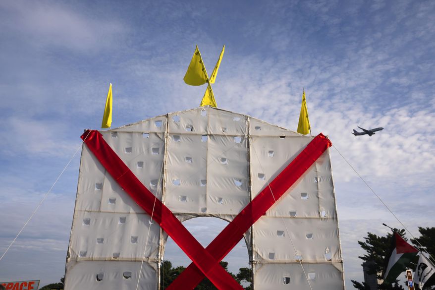 A plane flies over an anti-arch structure lifted up by demonstrators at Memorial Circle to protest the proposed Triumphal Arch, Thursday, Oct. 1, 2026, in Arlington, Va. (AP Photo/Allison Robbert)