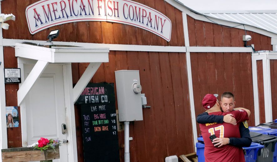 FILE - A man hugs a police officer in front of the American Fish Company following a fatal shooting that occurred the night before, Sept. 28, 2025, in Southport, N.C. (AP Photo/Chris Seward, File)
