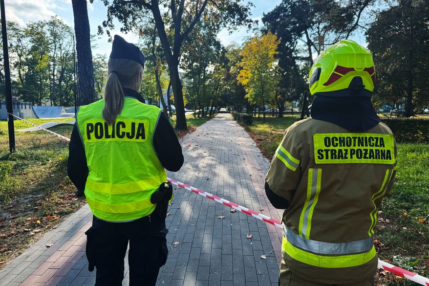 A police officer and a volunteer firefighter look down the street near a cordoned-off area following an attack on the Vocational School Complex No. 4 in Ostroleka, Poland, Wednesday, Oct. 7, 2026. (AP Photo/Rafal Niedzielski)