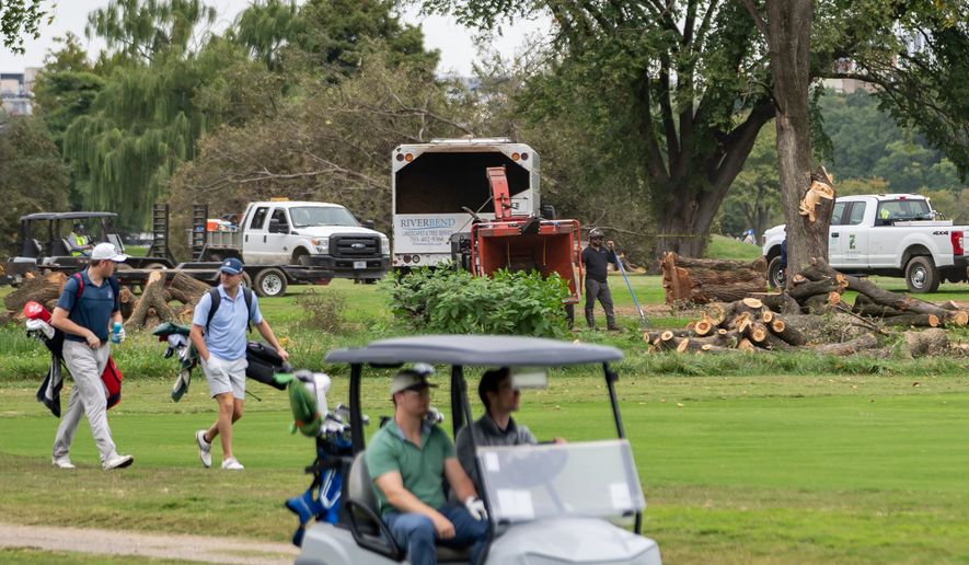 Golfers pass workers as the National Park Service begins cutting down trees at East Potomac Golf Links, Saturday, Oct. 10, 2026, in Washington. (AP Photo/Nathan Howard)