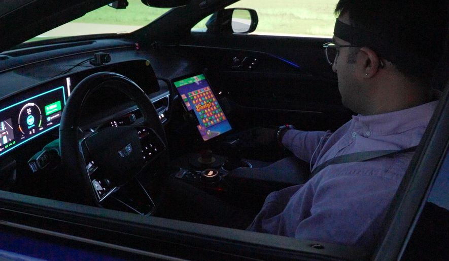 In this image from video, General Motors senior researcher Akilesh Rajavenkatanarayanan plays Candy Crush on a tablet mounted in a Cadillac Lyriq while it is in "eyes off" mode during a simulated drive at the automaker's Global Technical Center Friday, Sept. 18, 2026, in Warren, Mich. (AP Photo/Mike Householder)