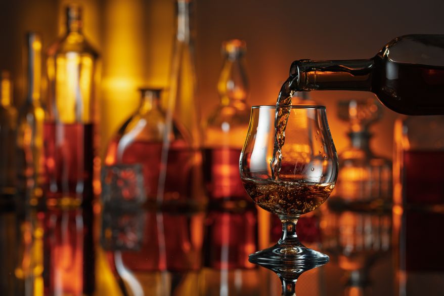 Pouring brandy from a bottle into a glass. Snifter of brandy on a black table in bar. Photo credit: Igor Normann via Shutterstock.