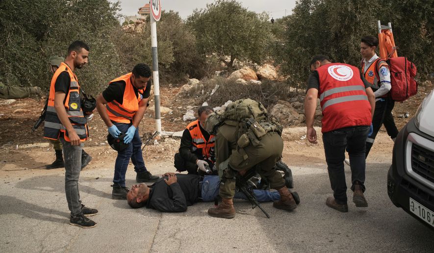 Palestinian medics and an Israeli soldier attend to a Palestinian man shot by Israeli soldiers following a settler attack on Palestinians harvesting olives in the West Bank village of Abu Falah, Friday, Oct. 16, 2026. (AP Photo/Leo Correa)