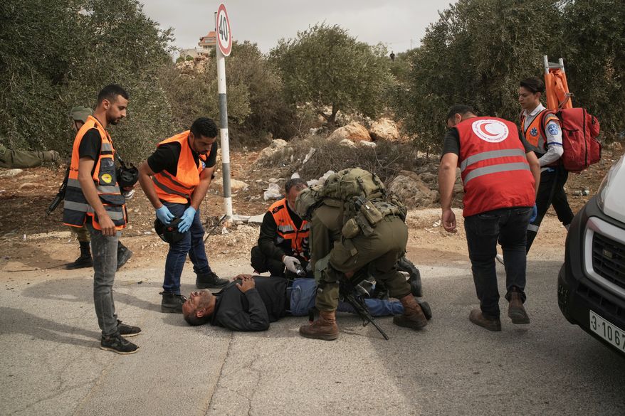 Palestinian medics and an Israeli soldier attend to a Palestinian man shot by Israeli soldiers following a settler attack on Palestinians harvesting olives in the West Bank village of Abu Falah, Friday, Oct. 16, 2026. (AP Photo/Leo Correa)