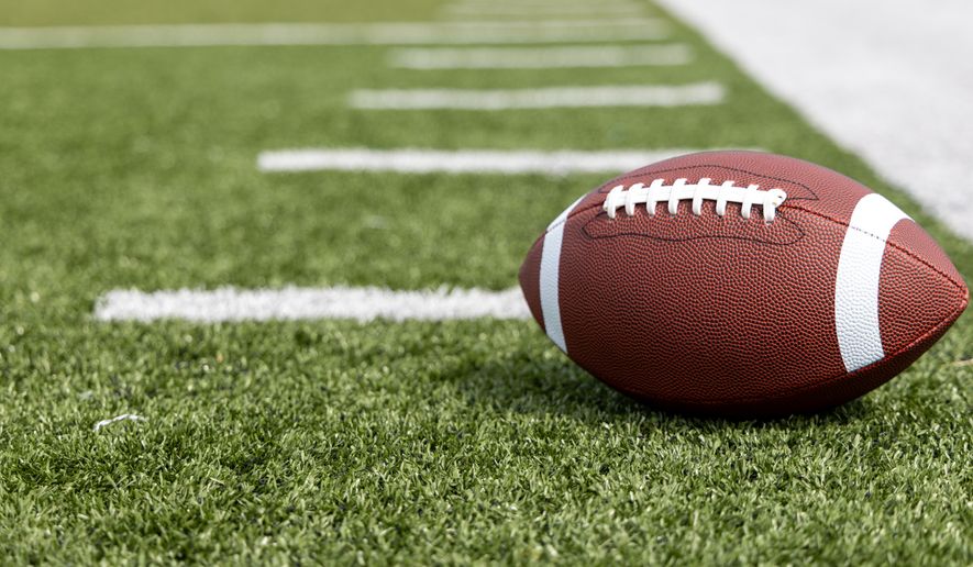Football sits on field dash lines. File photo credit: Donald Mroczkowski via Shutterstock.
