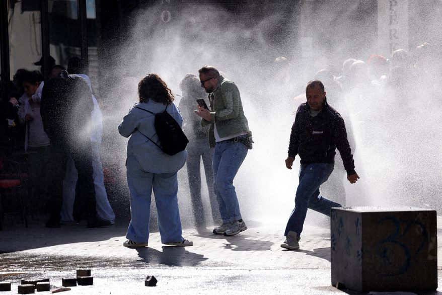 Protesters run from water sprayed by police water cannons during an anti-government demonstration outside the Education Ministry, in Tirana, Albania, Saturday, Oct. 17, 2026. (AP Photo/Hameraldi Agolli)