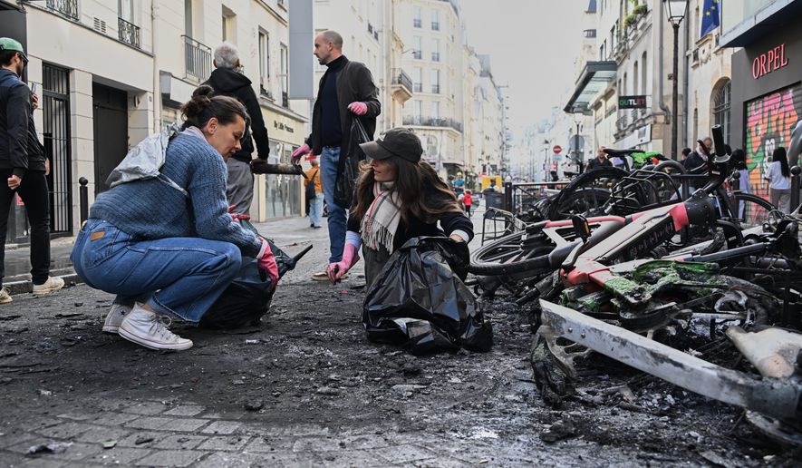 People clean up debris in a street next to burned bicycles the day after a demonstration against rising living costs and in solidarity with students' grievances, in Paris, Sunday, Oct. 18, 2026. (AP Photo/Emma Da Silva)