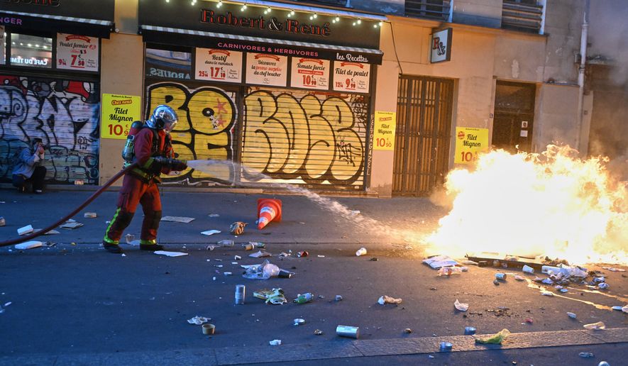 A firefighter extinguishes a fire during clashes with police a day after a demonstration against rising living costs, joining students' grievances, in Paris, Sunday, Oct. 18, 2026. (AP Photo/Emma Da Silva)