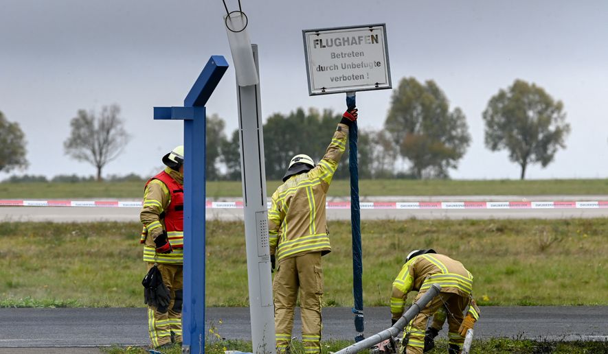 The airport's in-house fire department removes a sign that served as evidence at the spot where a vehicle crashed through the fence, as police are investigating a security incident at Leipzig/Halle airport, in Schkeuditz, Germany, Sunday Oct. 18, 2026. (Heiko Rebsch/dpa via AP)