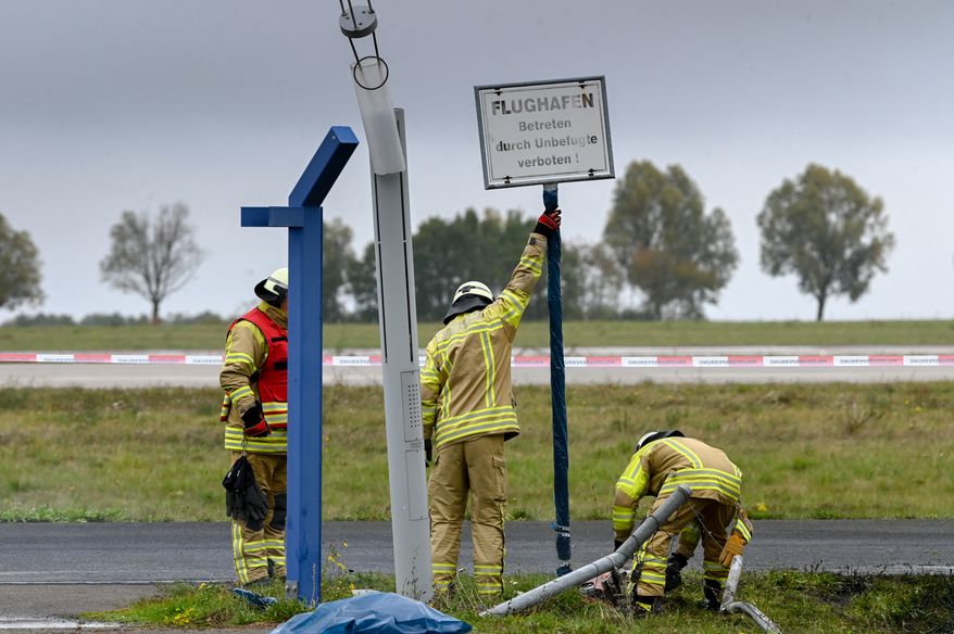 The airport's in-house fire department removes a sign that served as evidence at the spot where a vehicle crashed through the fence, as police are investigating a security incident at Leipzig/Halle airport, in Schkeuditz, Germany, Sunday Oct. 18, 2026. (Heiko Rebsch/dpa via AP)