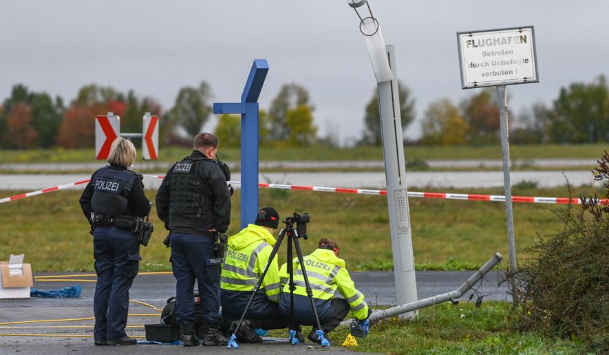 Police officers inspect the site of a damaged fence section at the entrance to the airport grounds, as they investigate a security incident at Leipzig/Halle airport, in Schkeuditz, Germany, Sunday Oct. 18, 2026. (Heiko Rebsch/dpa via AP)
