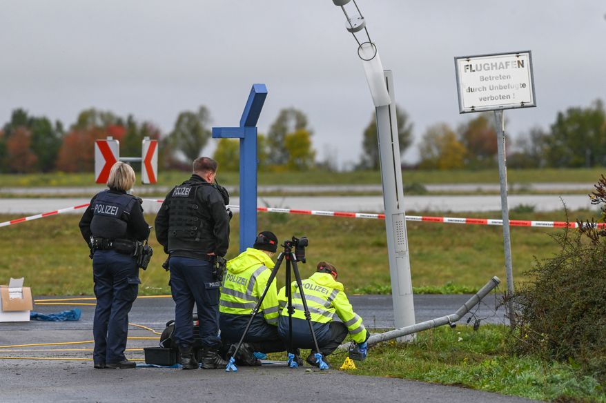 Police officers inspect the site of a damaged fence section at the entrance to the airport grounds, as they investigate a security incident at Leipzig/Halle airport, in Schkeuditz, Germany, Sunday Oct. 18, 2026. (Heiko Rebsch/dpa via AP)