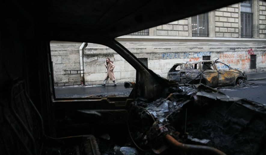A woman walks past burned-out cars after a quiet night Monday under curfew, the first since weekend protests over the cost of living turned into rioting and looting across France, in Paris, Tuesday, Oct. 20, 2026. (AP Photo/Christophe Ena)